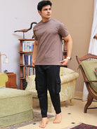 Man wearing a brown crew neck t-shirt and black pants in a living room setting