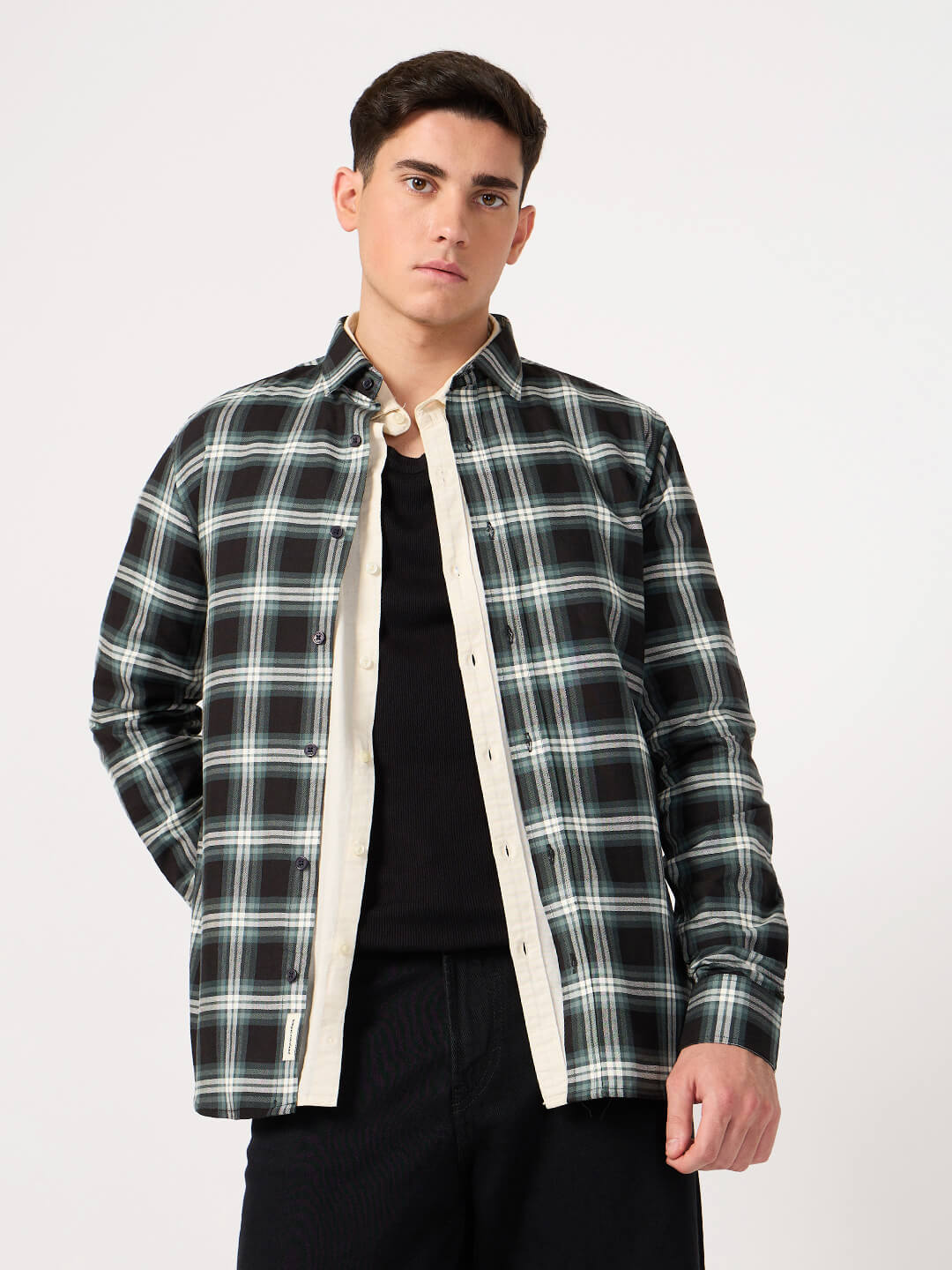 Man wearing a black and green plaid shirt over a black t-shirt on a white background