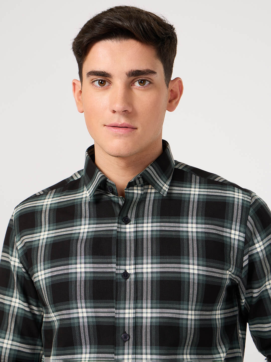 Man wearing a black and green plaid shirt made with pure cotton against a plain background