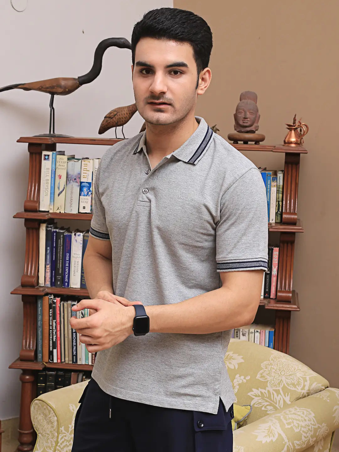 Man wearing a gray cotton polo shirt standing in front of a bookshelf.