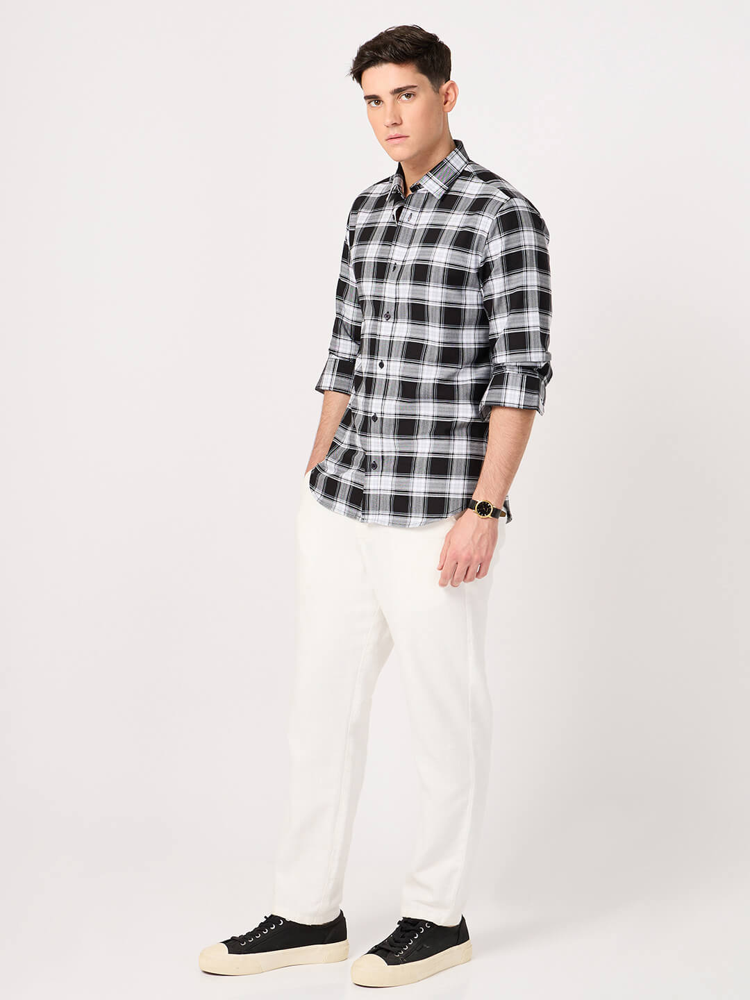Man wearing a black and white checkered shirt with white pants on a white background