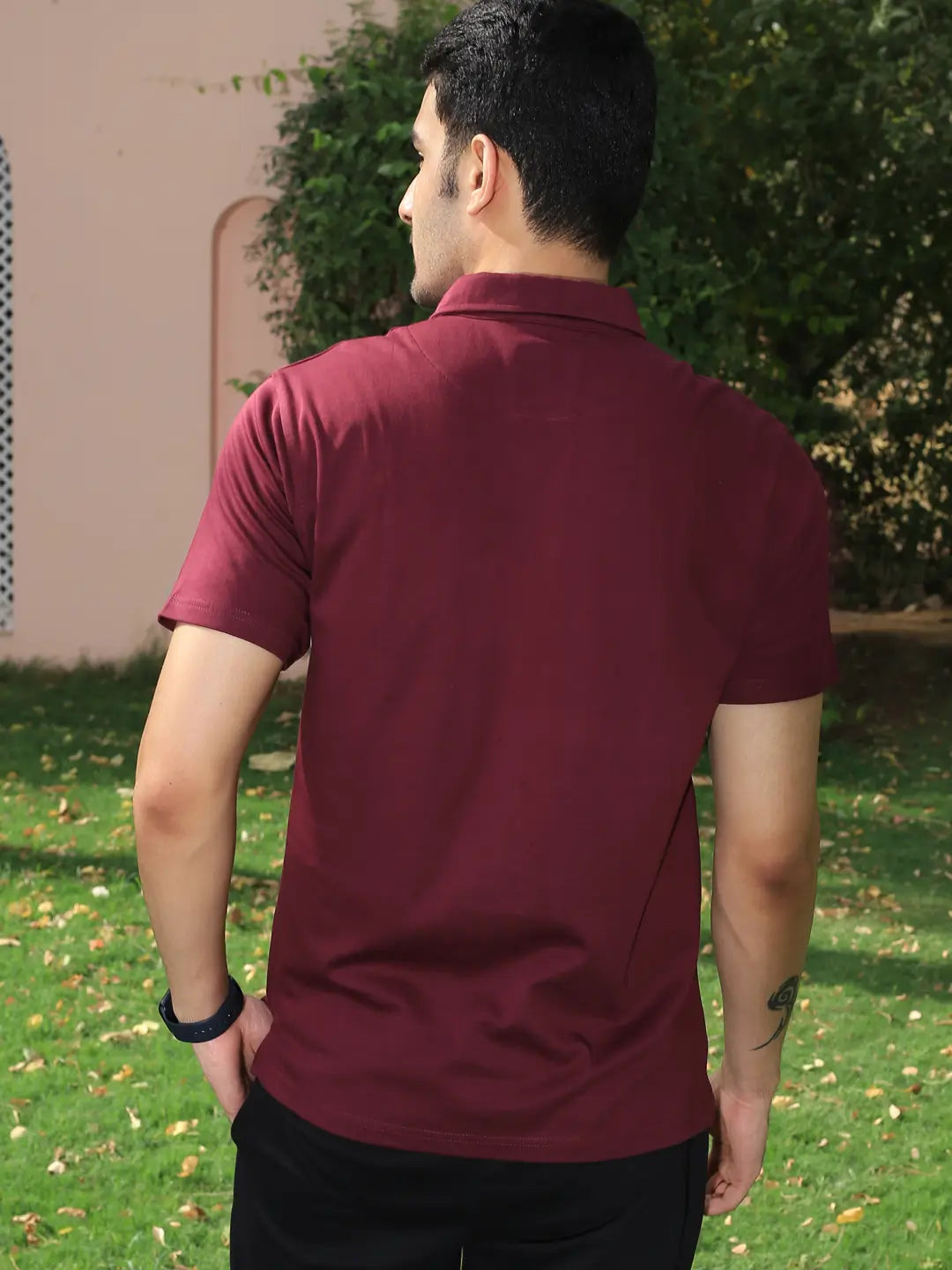 Man wearing a maroon cotton polo t shirt standing outdoors on grass with trees in the background