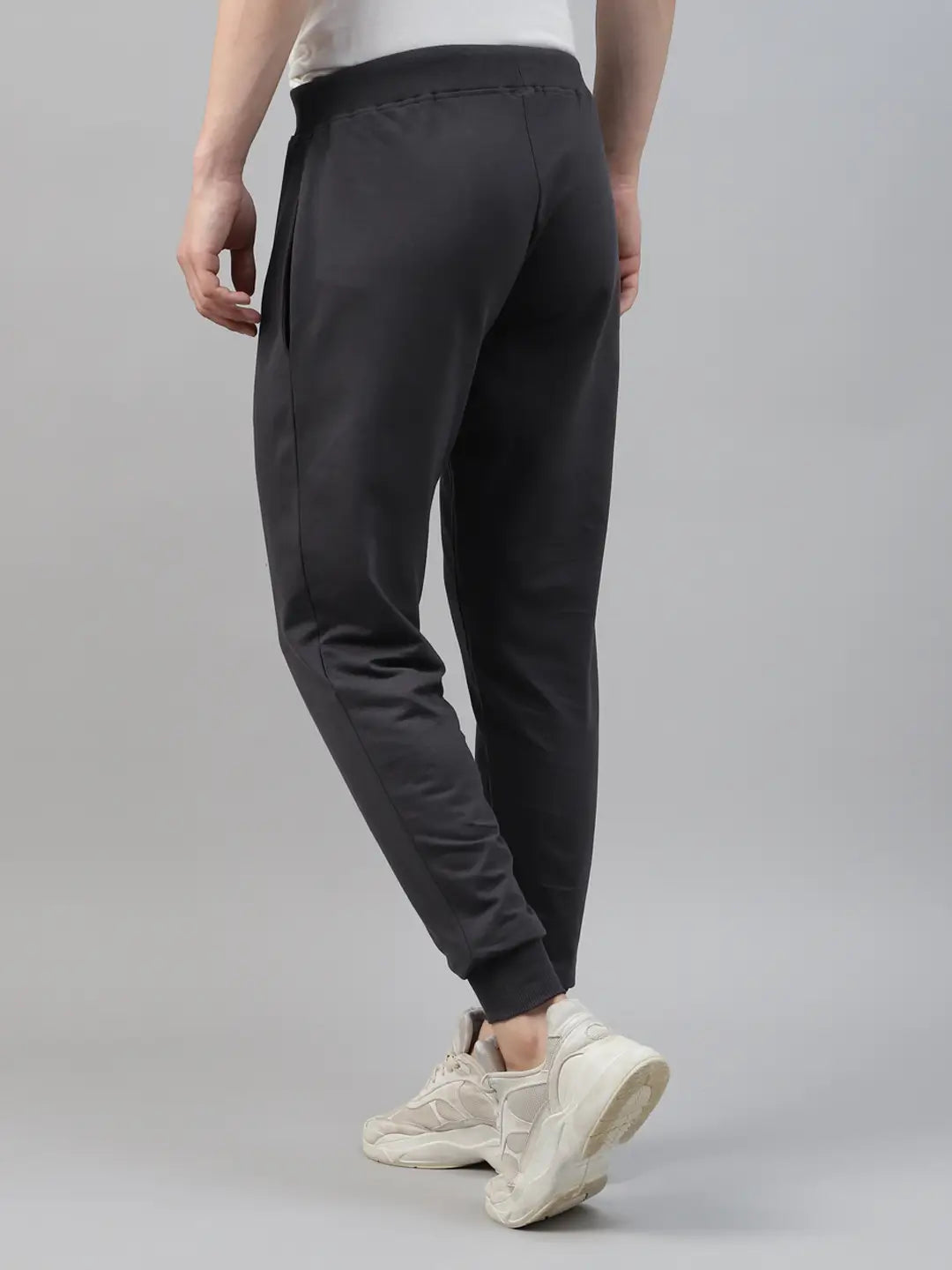 Person wearing dark grey jogger pants and white sneakers on a gray background