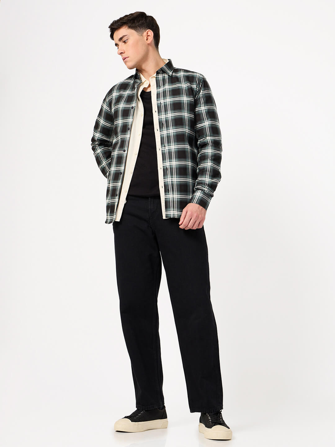 Man wearing a black and green plaid shirt over a black t-shirt with black pants on a white background