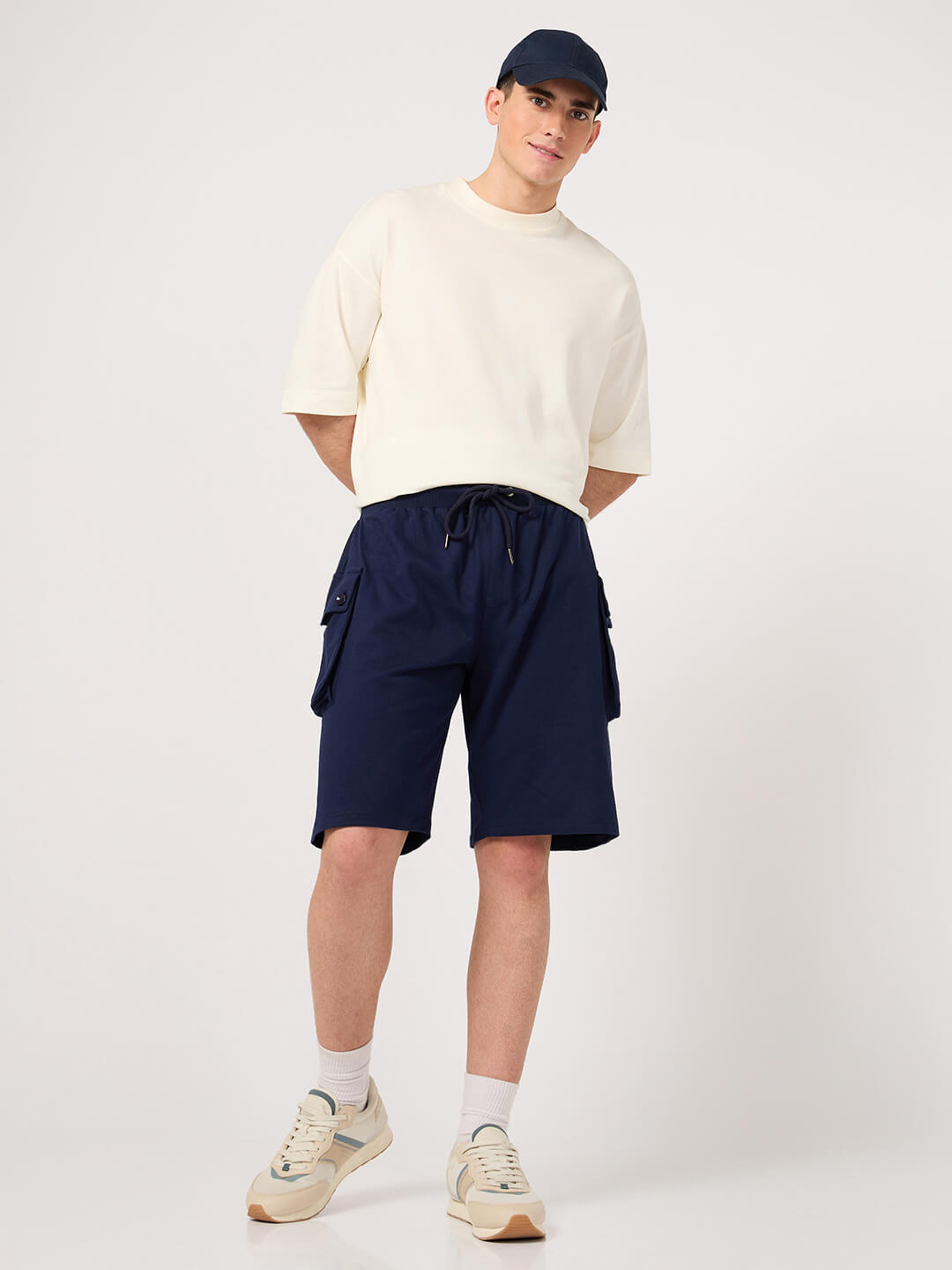 Person wearing a white shirt, navy shorts, and a cap on a white background