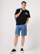 Man wearing a black printed t-shirt, blue denim shorts, and black sneakers on a white background