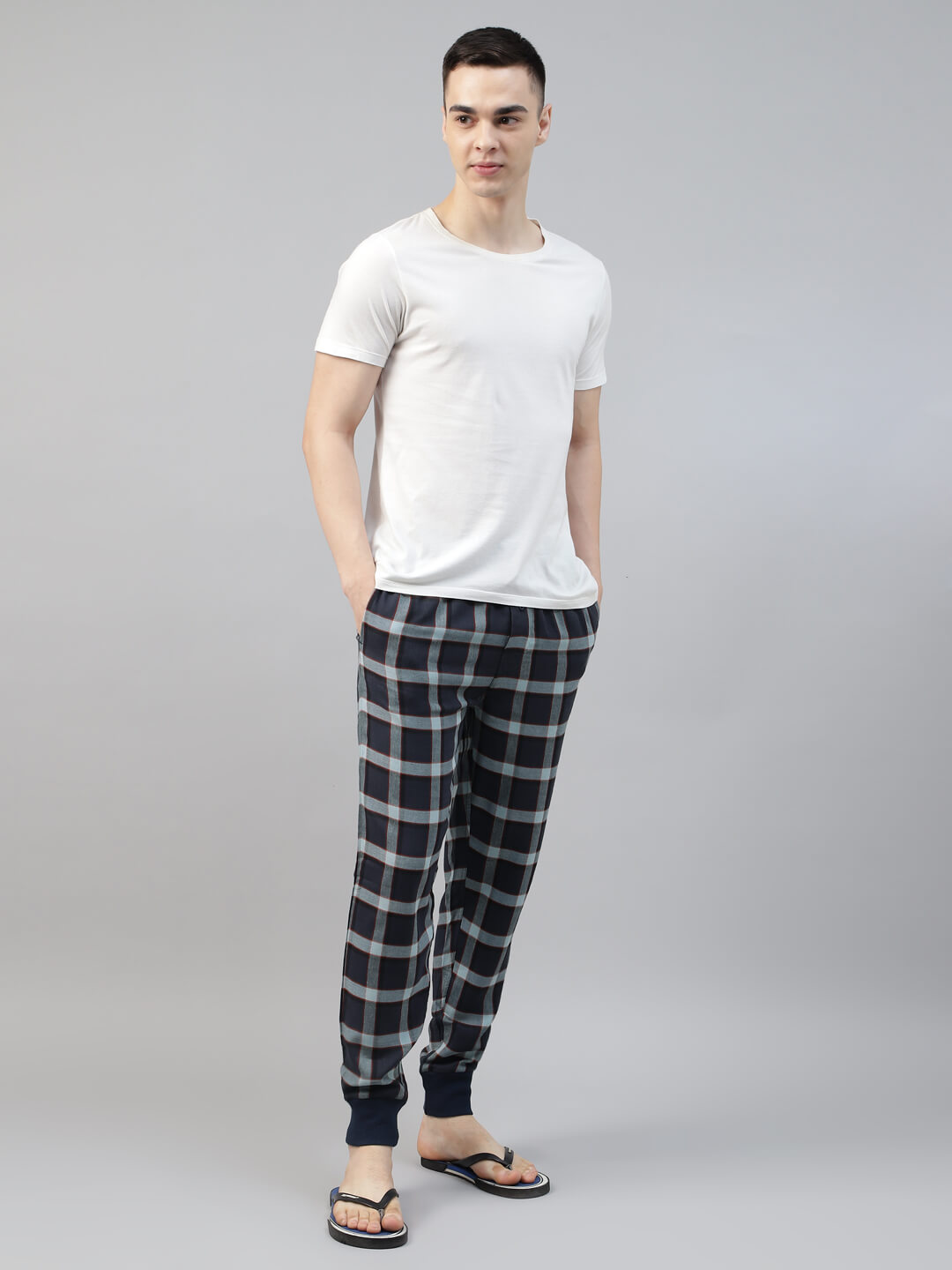 Man wearing a white t-shirt and black plaid jogger pants on a gray background