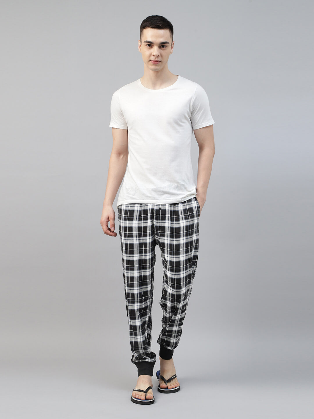 Man wearing a white t-shirt and black and white checkered pants on a gray background