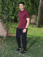 Man wearing a maroon polo shirt and black pants standing outdoors on grass with trees in the background