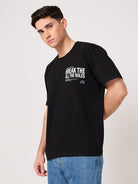 Person wearing a black t-shirt with printed text on a plain background
