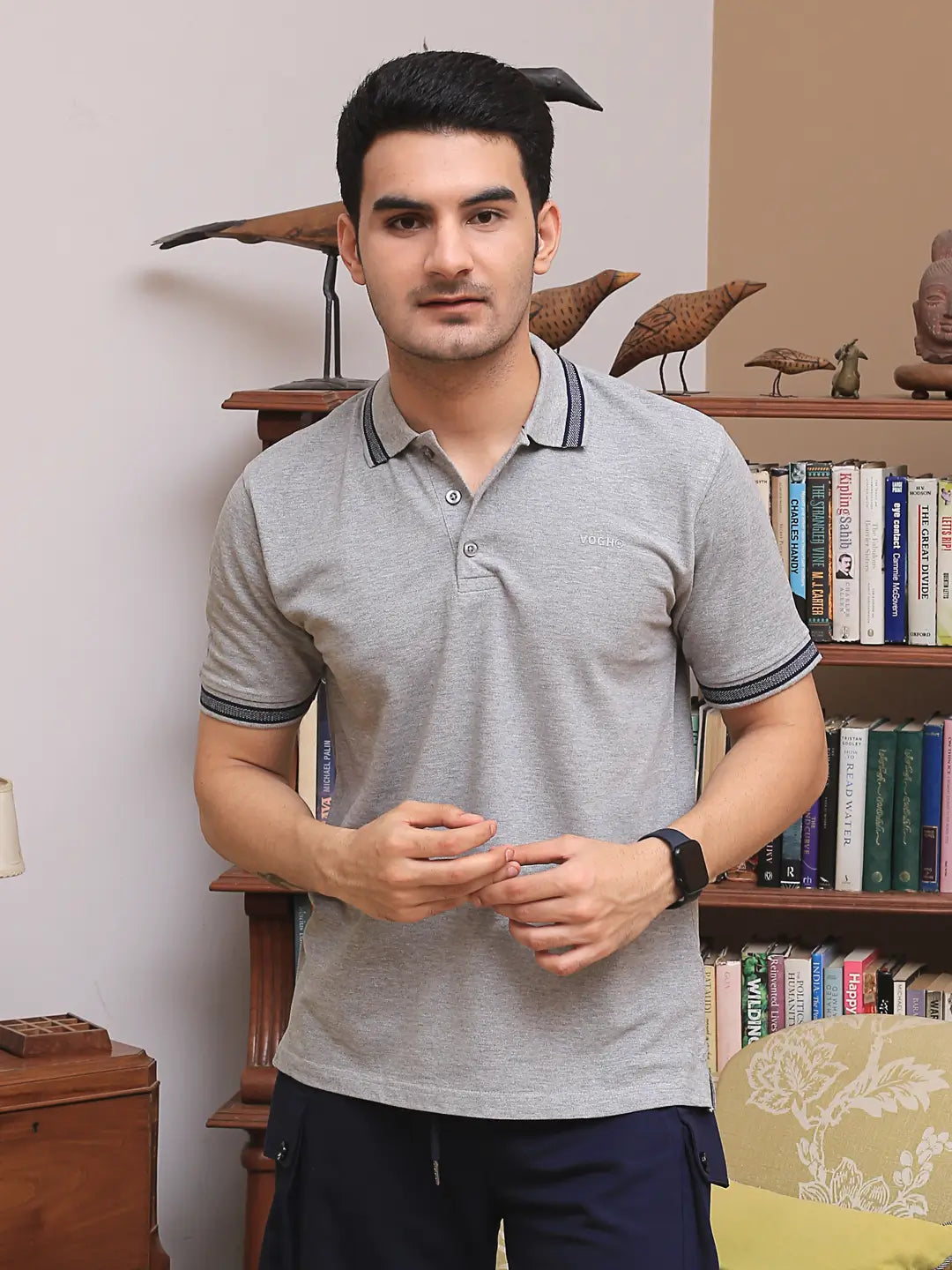 Man wearing a gray cotton polo t shirt standing in front of a bookshelf.