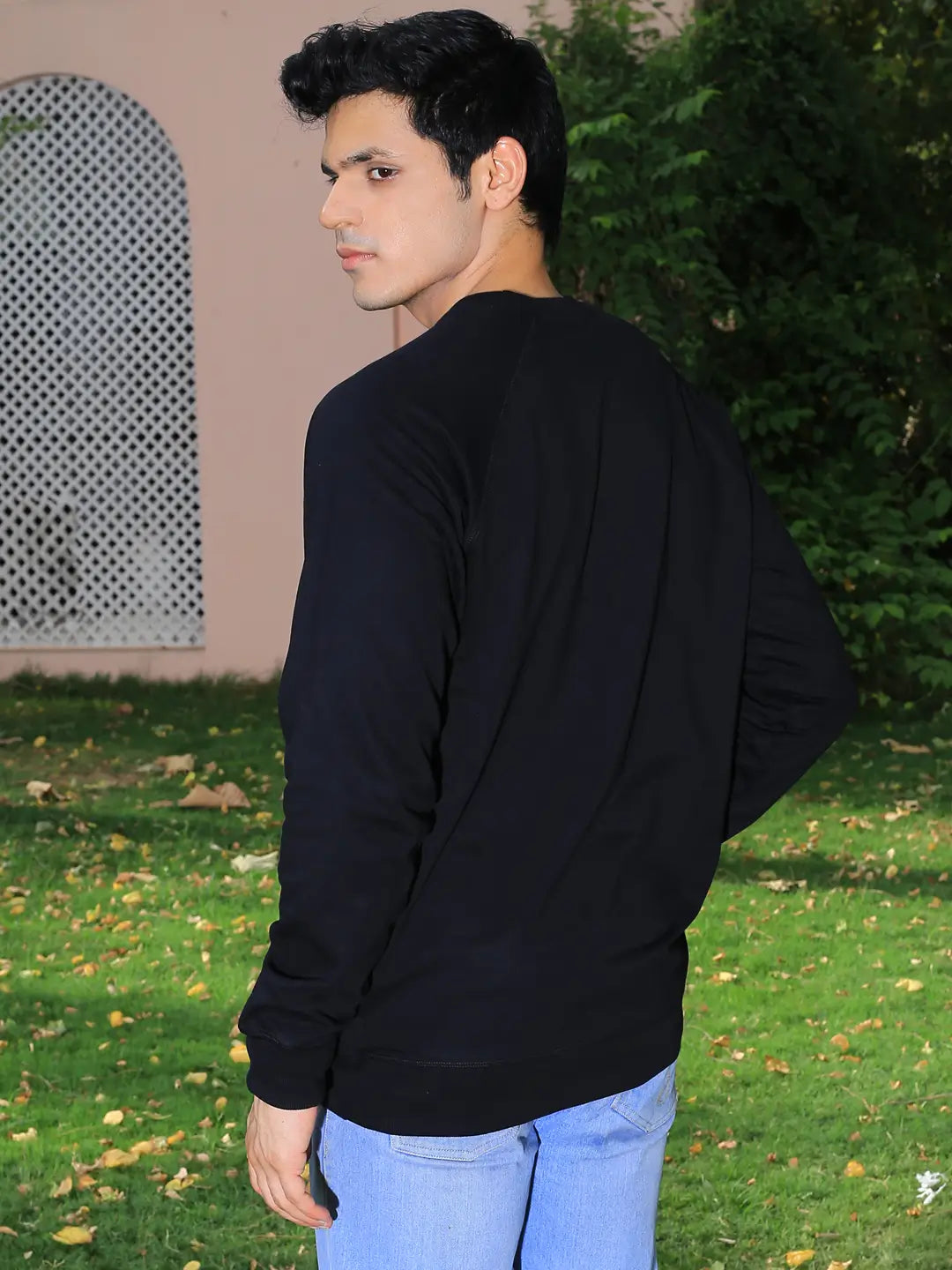 Man wearing a black sweatshirt and light blue jeans standing outdoors