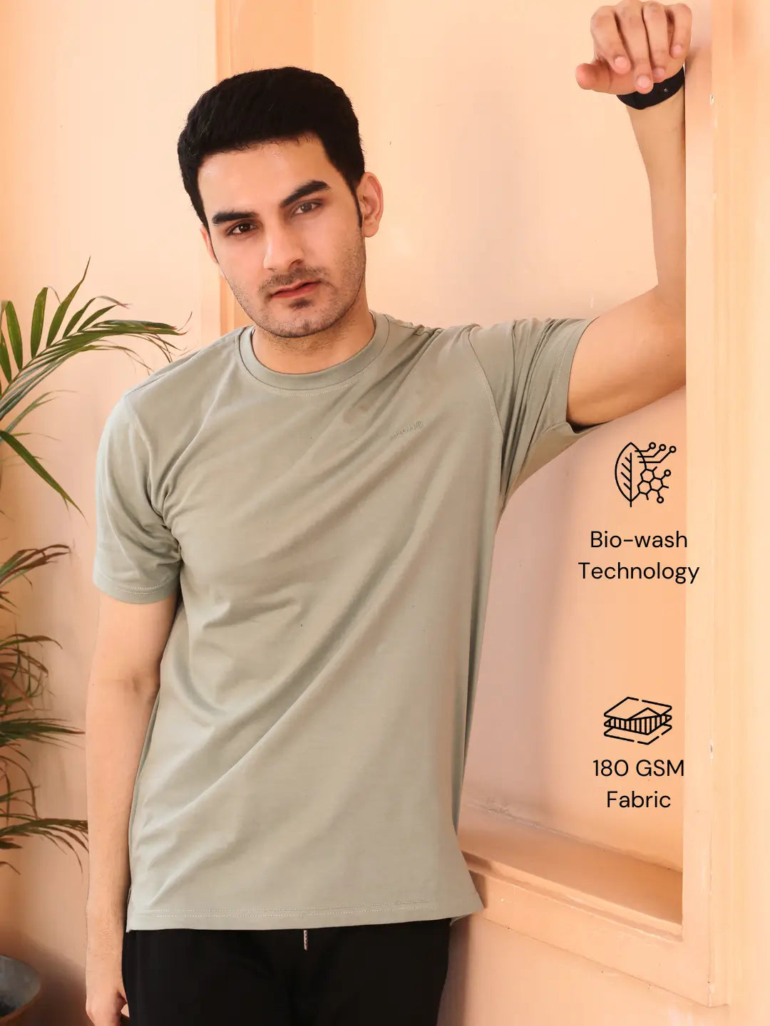 Man wearing a light gray crew neck cotton t-shirt, standing against a beige wall.