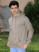 Man wearing a light grey hoodie outdoors with greenery in the background