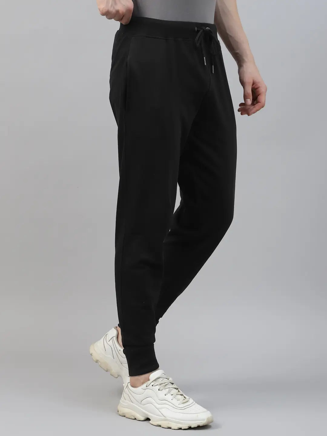 Person wearing black jogger pants and white sneakers on a gray background