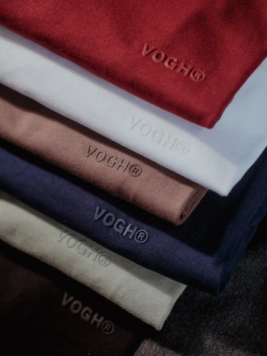Stack of folded cotton t shirts with 'VOGH' branding in various colors.