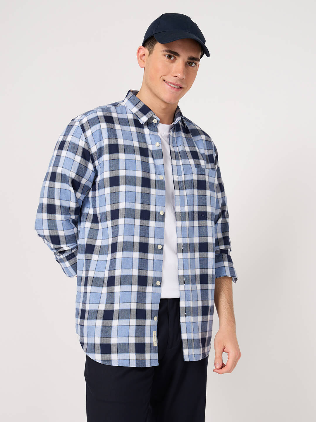 Man wearing a blue and white checkered shirt with a navy cap on a light gray background