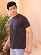 Man wearing a dark gray crew neck t-shirt standing indoors with a plant in the background