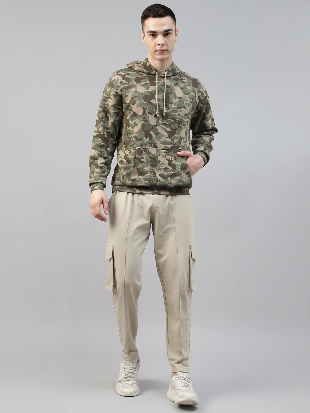 man wearing a army print hoodie and beige cargo jogger pants on a gray background